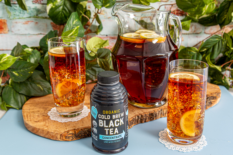 A pitcher and glasses of Trader Joe's Organic Cold Brew Black Tea Concentrate next to product in packaging