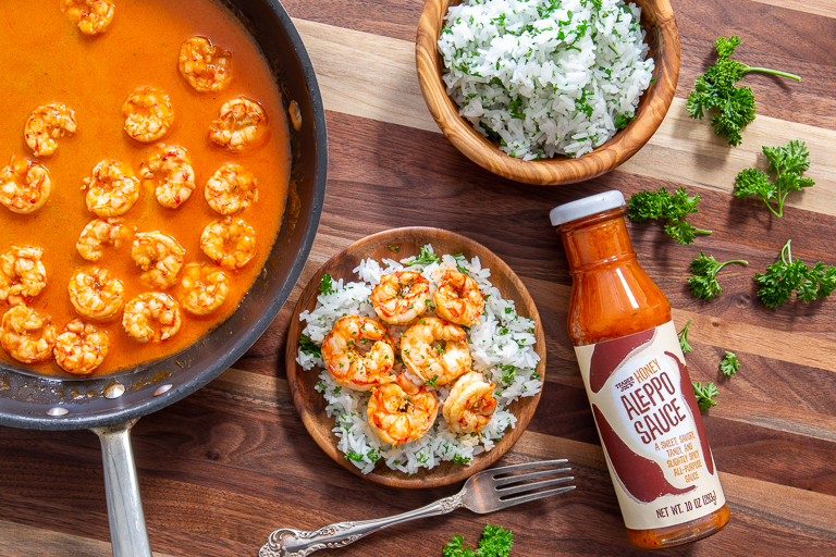 Pan of shrimp simmered in Trader Joe's Honey Aleppo Sauce, next to a plate of rice topped with shrimp